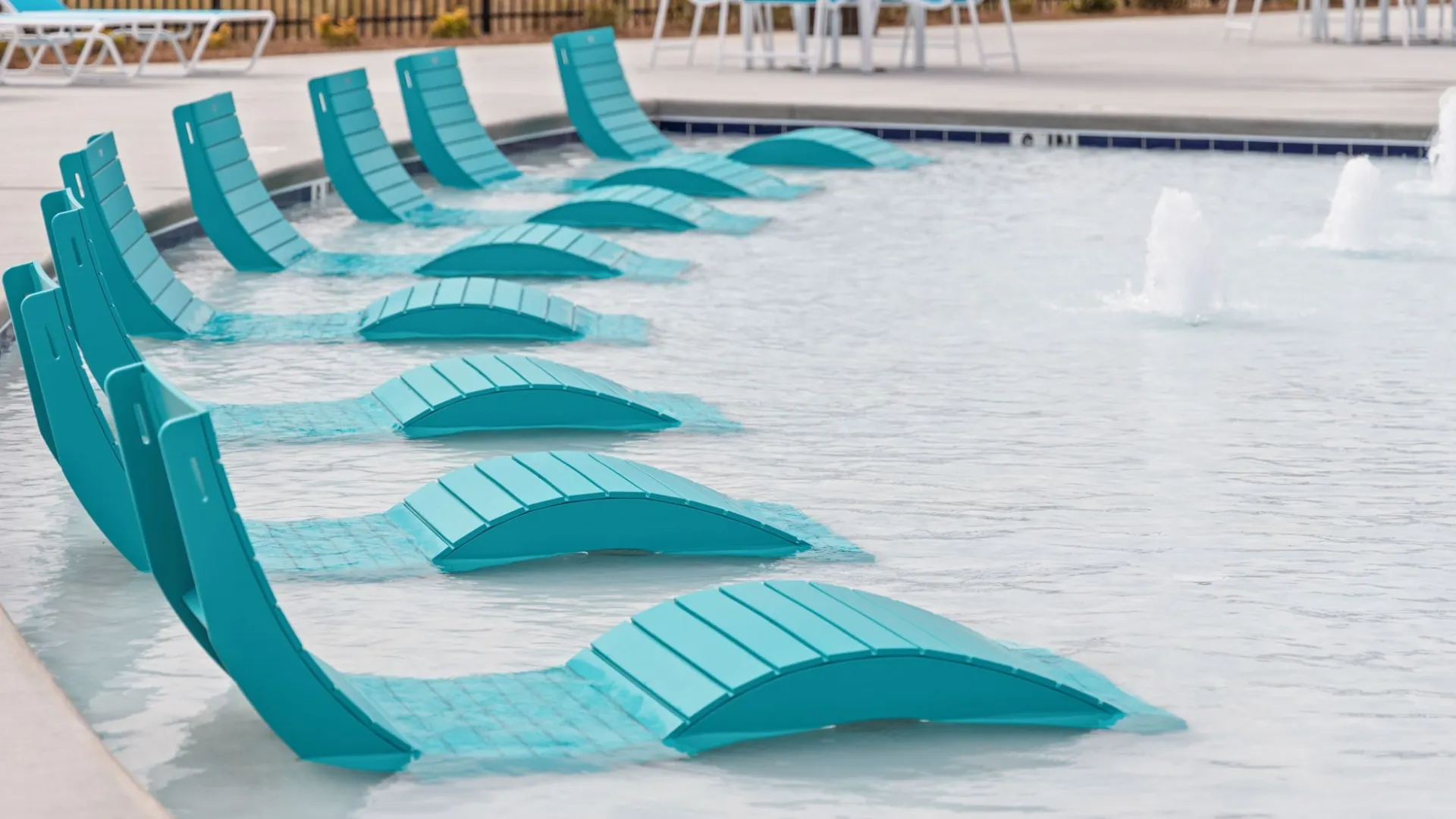 Turquoise pool lounge chairs partially submerged in shallow water at a sunny outdoor swimming pool.