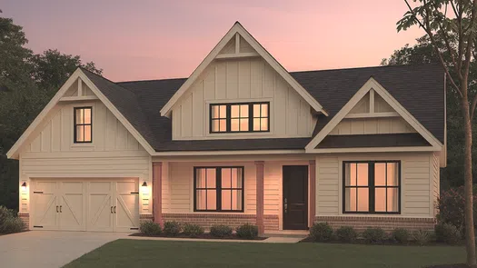Modern farmhouse style house with warm lights at sunset and a two-car garage on a green lawn